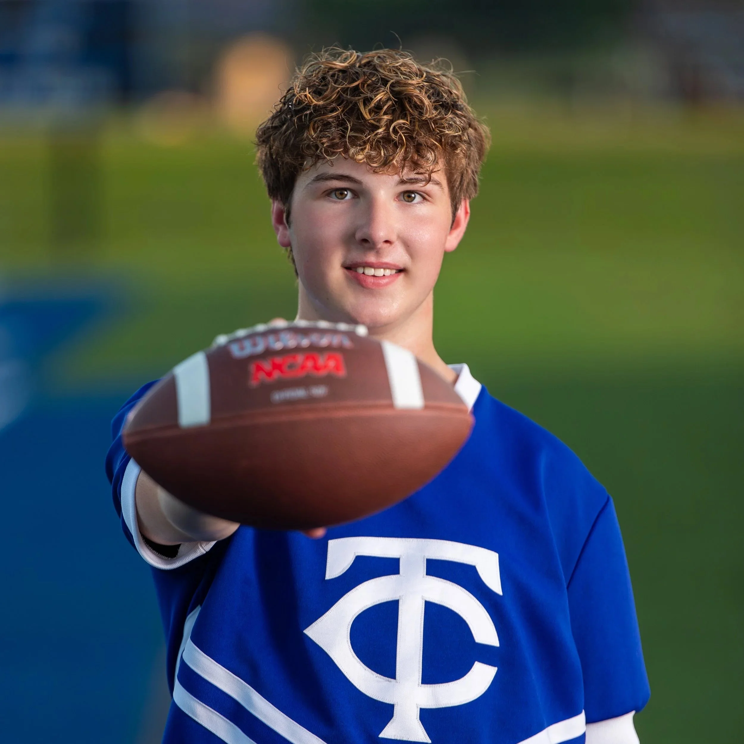 A Tuscaloosa County football player in a blue jersey holding out a football on the field.